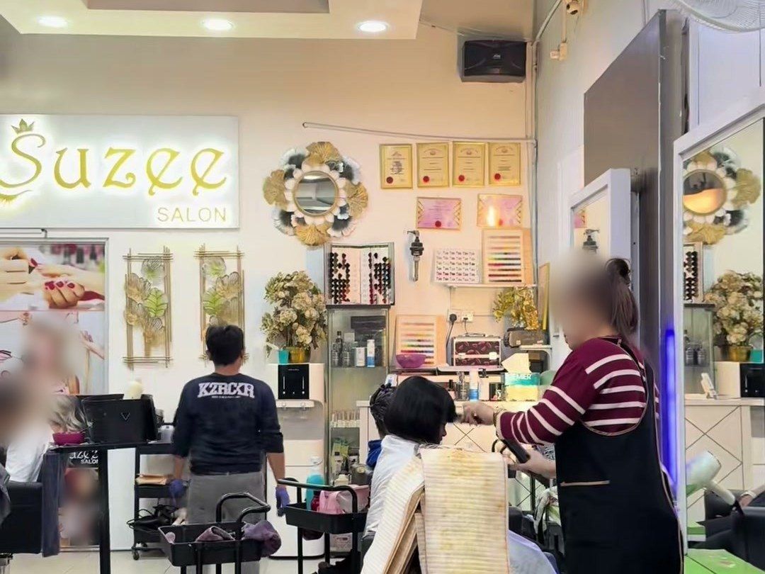 Ruang dalam Suzee Salon dengan papan tanda Suzee bercahaya, carta warna dan staf sedang bekerja; wajah dikaburkan